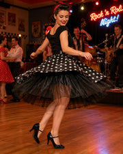 Frau im Rockabilly-Kleid wirbelt tanzend über die Tanzfläche, während eine Liveband bei einer Rock’n’Roll-Nacht spielt.